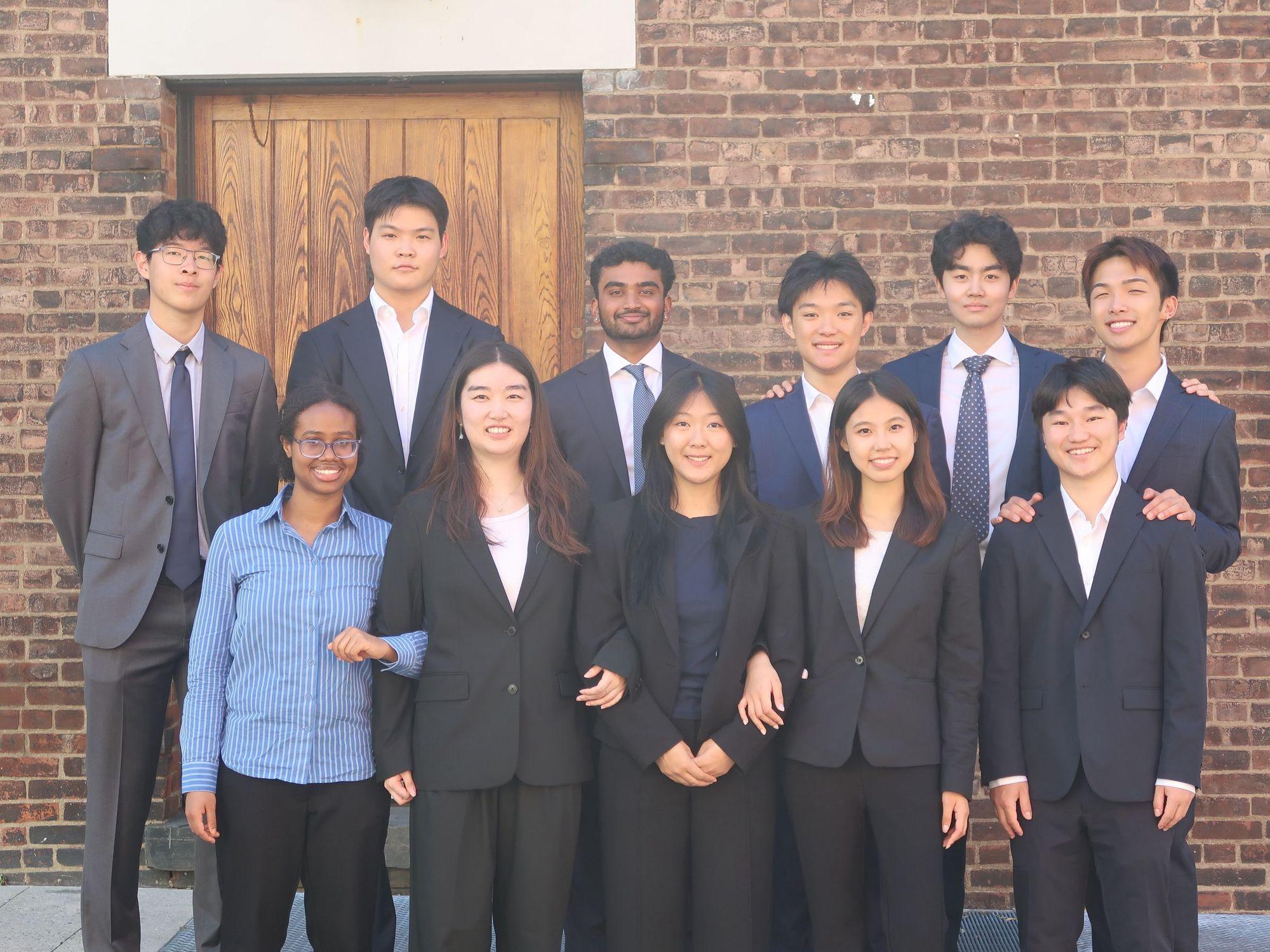 The GRC at NYU executive board standing together in front of a brick wall and wooden door