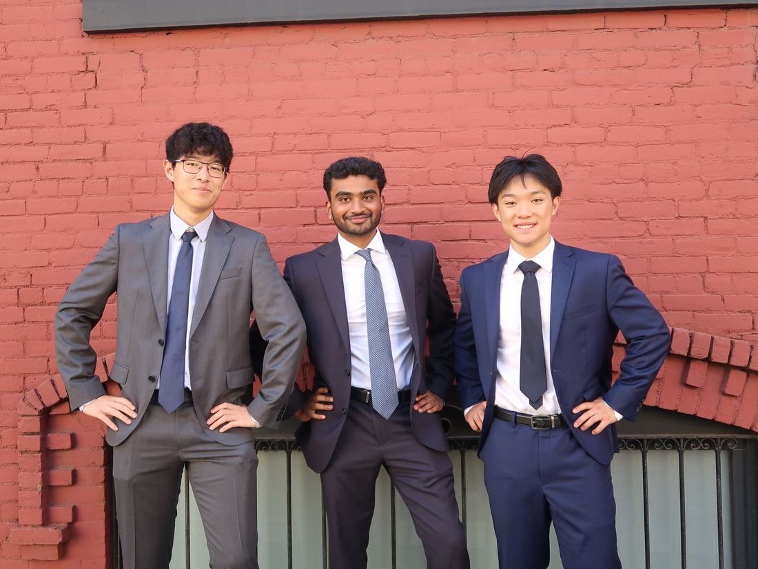 Three members of the consulting team posing together in suits against a red brick wall
